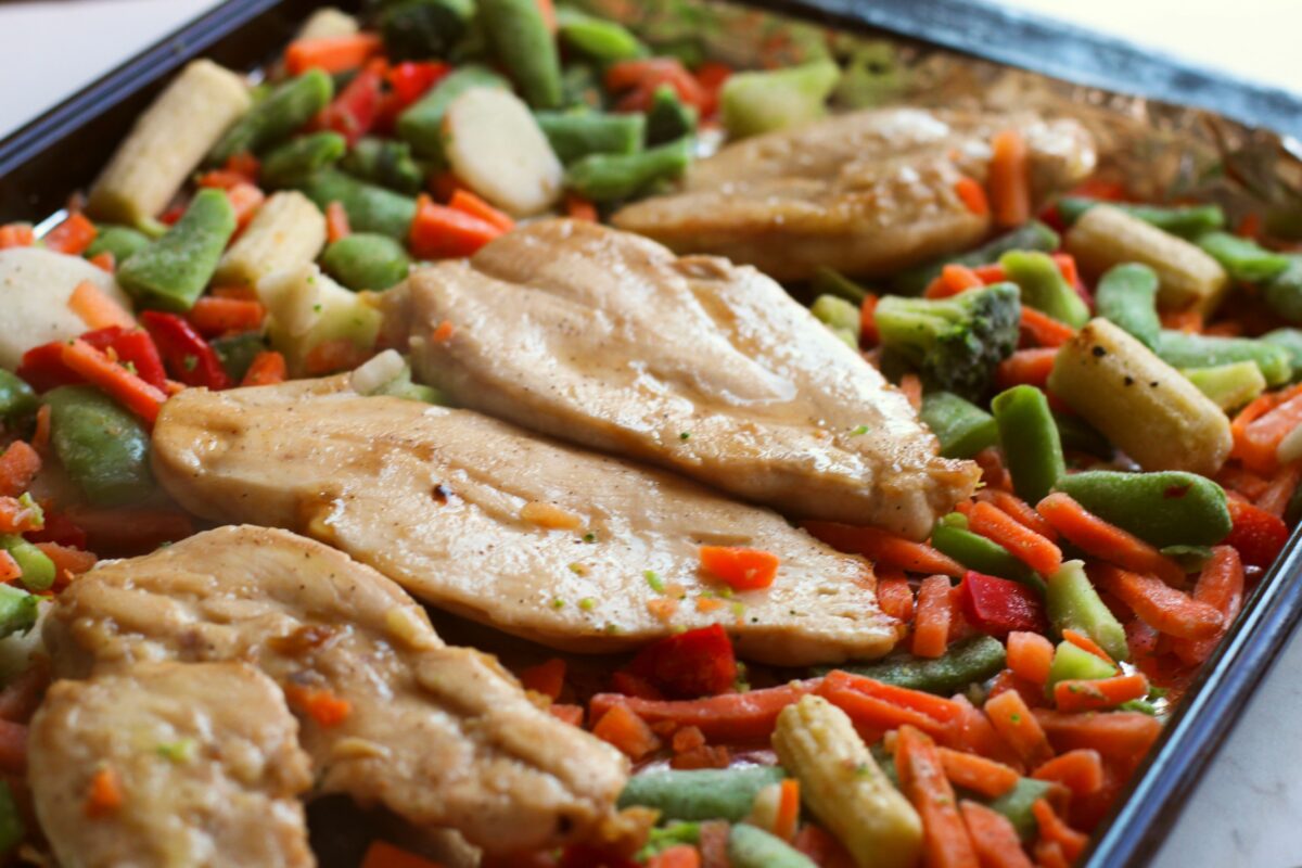 Chicken breasts partially baked, with veggies on the sheet pan.