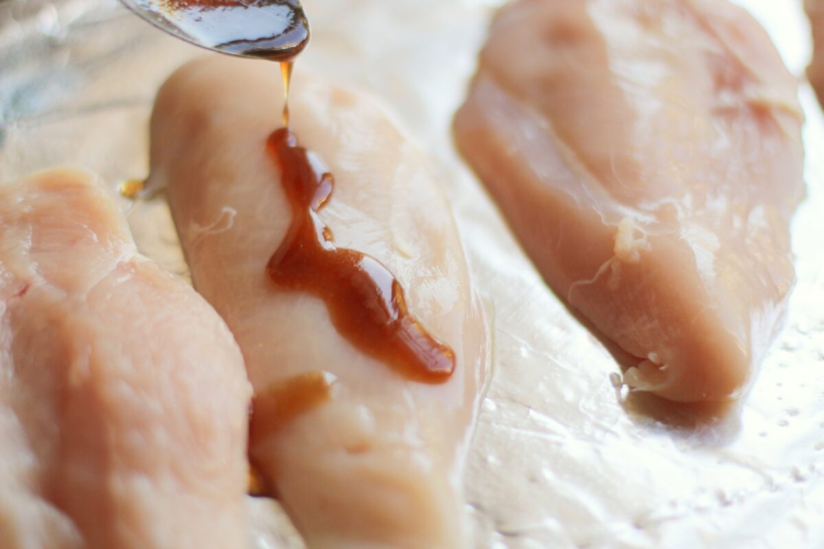 Drizzling teriyaki sauce over uncooked chicken breasts on a foil lined baking sheet,