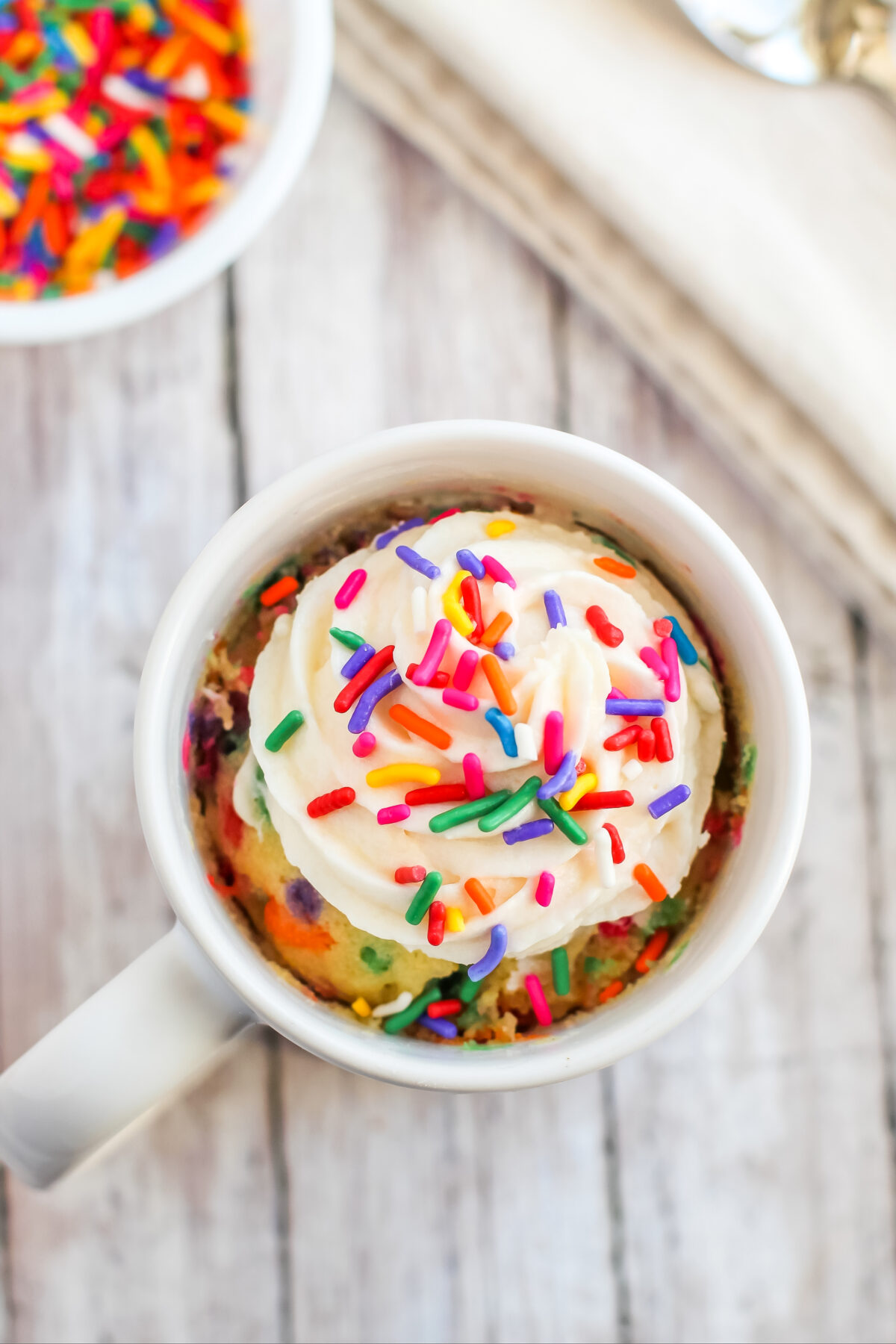 A sweet and simple vanilla funfetti mug cake recipe for the microwave! It's fluffy and moist, and topped with a dollop of buttercream!