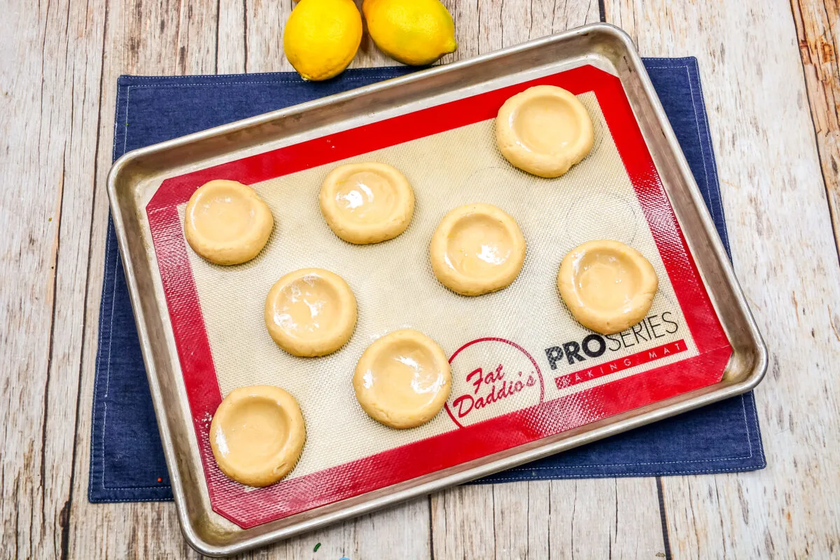 Flattened dough balls on a baking sheet lined with a silicone liner.