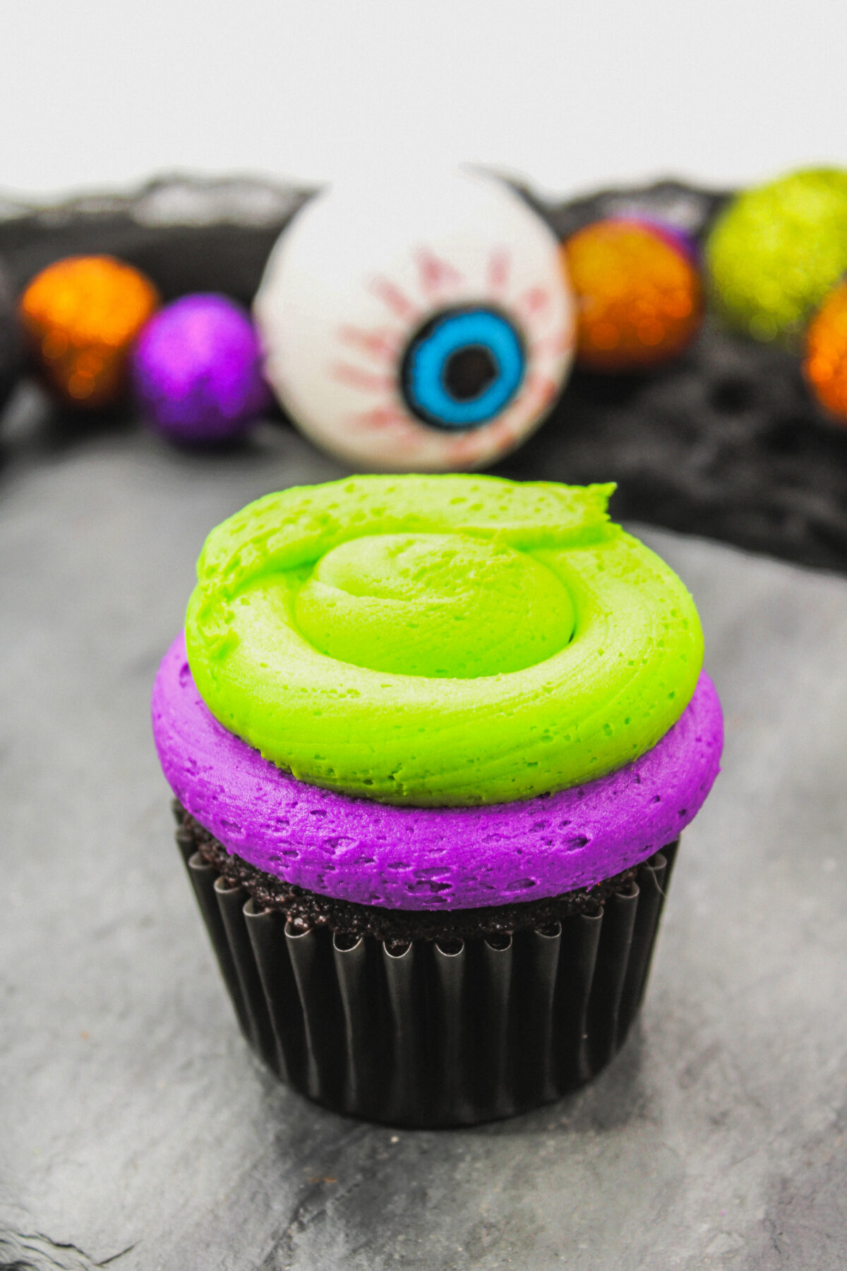 Cupcake with a layer of green frosting on top of the purple frosting.