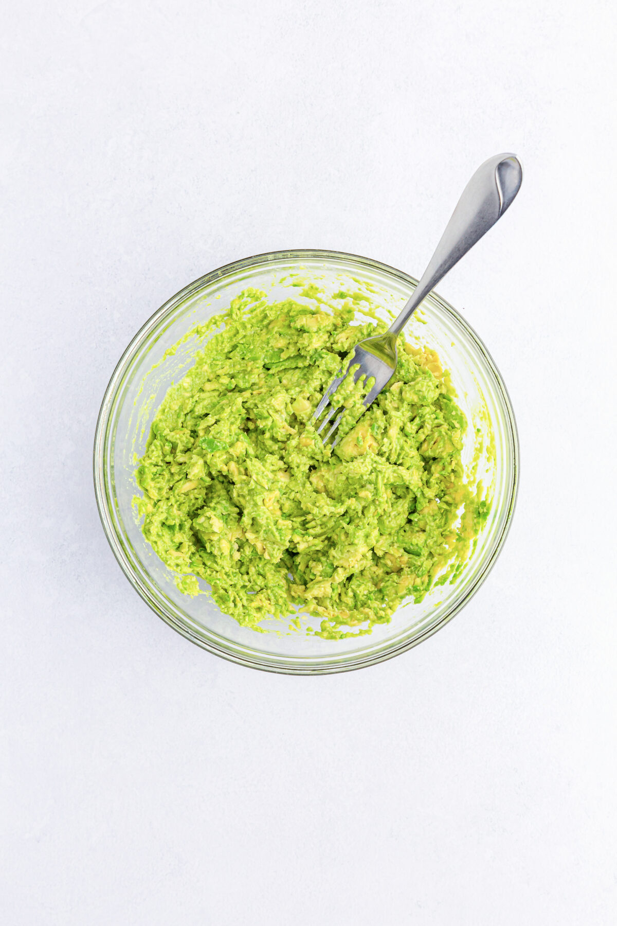 Avocado mashed with a fork in a glass bowl.